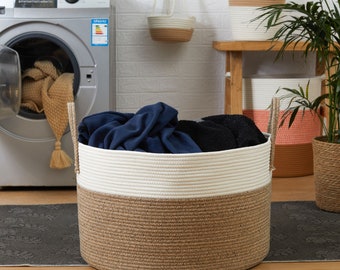 May include: A large, round laundry basket made of woven rope. The basket is two-toned, with a natural brown base and a cream-colored top. It is filled with dark blue and black clothing. The basket has two rope handles.