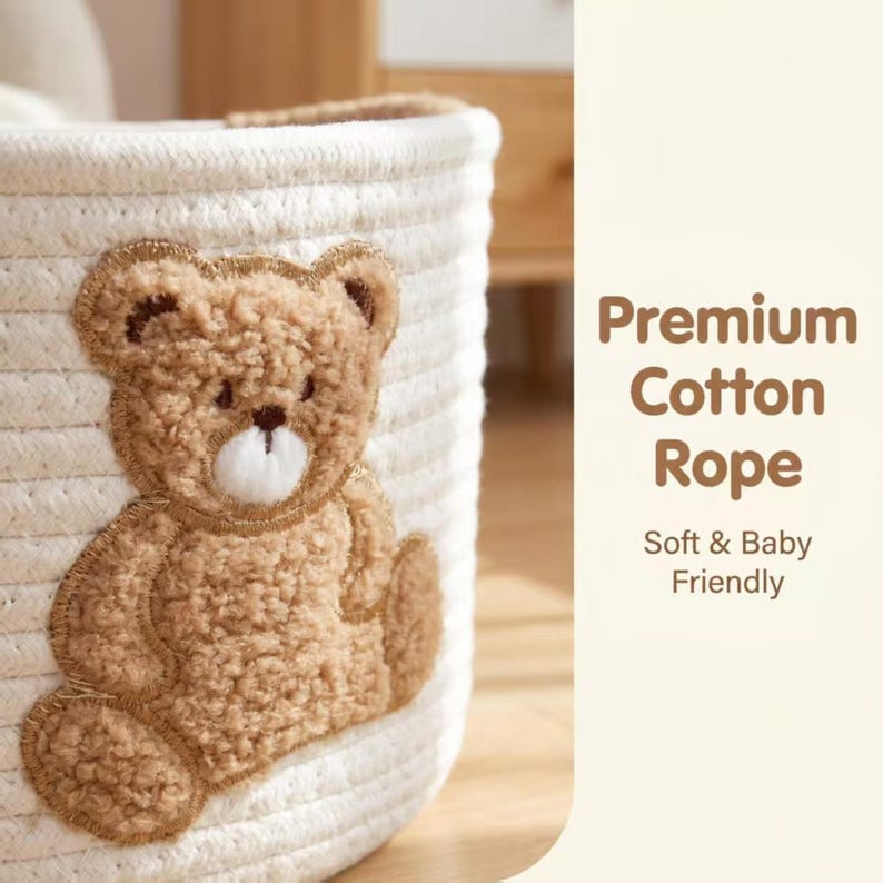 Pode incluir: Um cesto de armazenamento de corda de algod&atilde;o branco com uma aplica&ccedil;&atilde;o de urso de peluche castanho. O texto na lateral diz "Premium Cotton Rope" e "Soft & Baby Friendly". O cesto &eacute; projetado para artigos de beb&ecirc;.