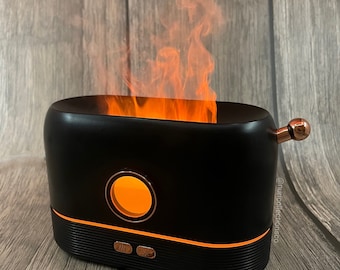 May include: Black electric essential oil diffuser with a glowing orange light and a simulated flame effect. The diffuser has a round opening and three buttons on the front. The text "@nurcollectionco" is visible on the side.