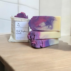 May include: Three bars of handmade soap in a purple and white swirl pattern. The soap is packaged in a white muslin bag with a label that reads "Black Raspberry & Vanilla" and "100% Handcrafted 120 ml | 4 oz."