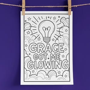 May include: A black and white coloring page with the text "GRACE GOT ME GLOWING" and an illustration of a lightbulb, stars, and clouds. The page is hanging from a string with wooden clothespins against a purple background.