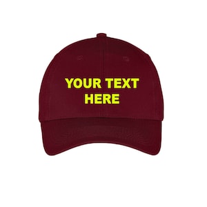 May include: A maroon baseball cap with a yellow embroidered text that says "YOUR TEXT HERE".
