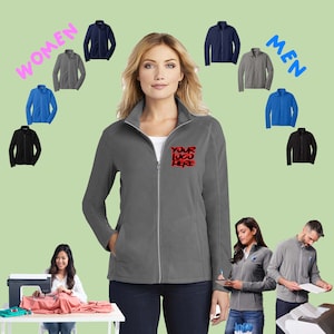 May include: A gray fleece jacket with a zipper closure and two pockets. The jacket has the text "YOUR LOGO HERE" embroidered on the left chest. The jacket is shown on a model, with other jackets in various colors displayed in the background.