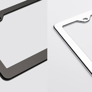 May include: Two license plate frames, one black and one chrome. Both frames have a rounded edge and a hole in the top center.
