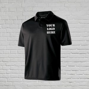 Puede incluir: Polo negro con mangas cortas y cuello. La camiseta presenta el texto "YOUR LOGO HERE" en letras blancas en el pecho. La camisa está hecha de una tela suave, probablemente sintética.
