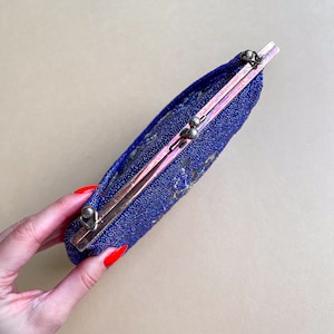 K&ouml;nnte beinhalten: Eine blaue Perlen-Abendtasche mit einem silbernen Verschluss. Die Tasche ist geschlossen und hat einen dezenten irisierenden Glanz.