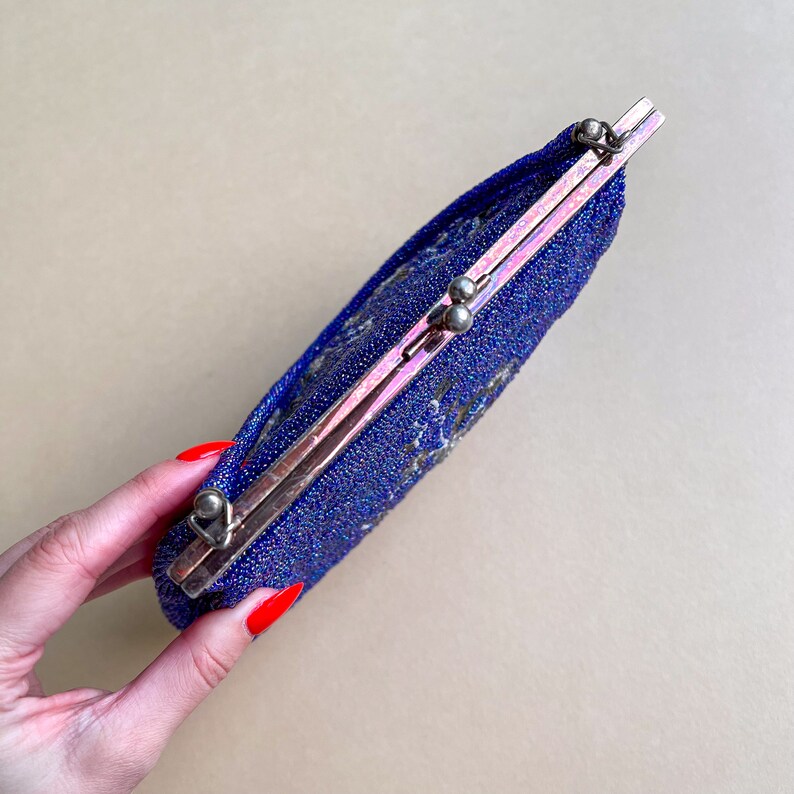 K&ouml;nnte beinhalten: Eine blaue Perlen-Abendtasche mit einem silbernen Verschluss. Die Tasche ist geschlossen und hat einen dezenten irisierenden Glanz.