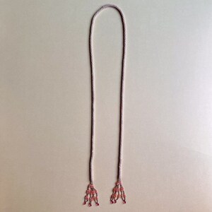May include: A long, thin, beaded necklace with pink and white beads. The necklace has two tassels at the ends, each with pink and white beads.