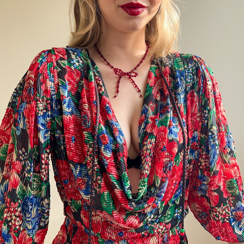 K&ouml;nnte beinhalten: Eine rote Perlenkette mit einem Schleifenanh&auml;nger, getragen &uuml;ber einem schwarzen und roten Blumenkleid mit einem Cowl-Ausschnitt.