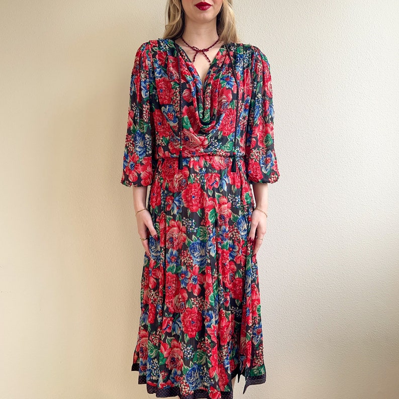 K&ouml;nnte beinhalten: Ein rotes, blaues und schwarzes Blumenkleid mit einem Cowl-Ausschnitt und einem langen Rock. Das Kleid hat einen schwarzen Besatz am Ausschnitt und an den &Auml;rmeln.