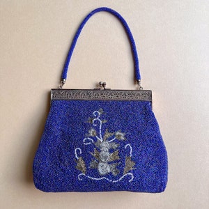 K&ouml;nnte beinhalten: Eine blaue Perlen-Abendtasche mit einem silbernen Verschluss und floraler Stickerei. Die Tasche hat einen oberen Henkel und einen Verschluss.