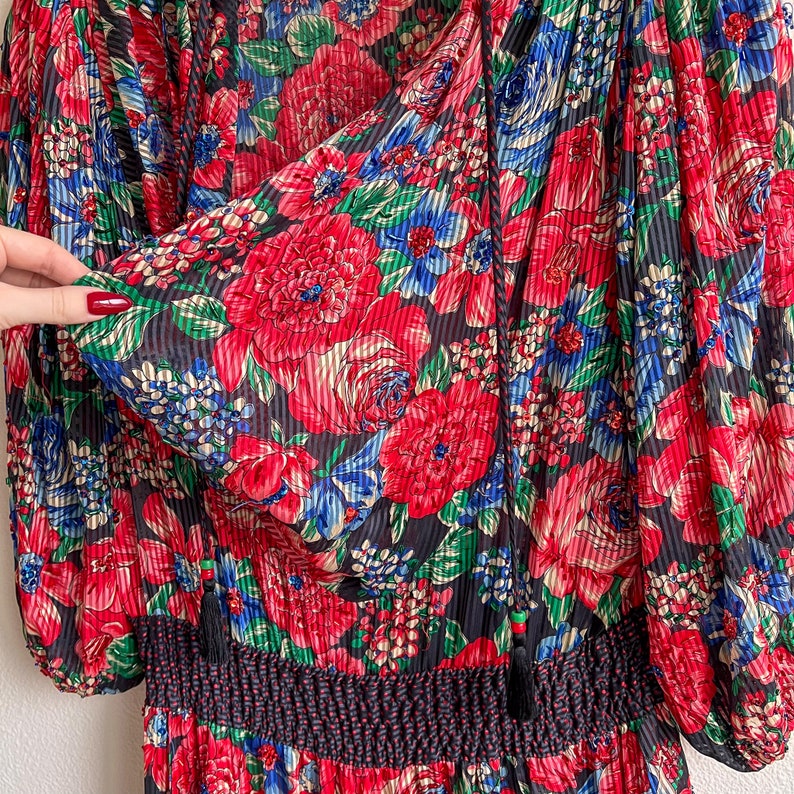 K&ouml;nnte beinhalten: Ein schwarzes, rotes und blaues Blumenkleid mit geraffter Taille und langen &Auml;rmeln. Das Kleid ist aus einem leichten, durchsichtigen Stoff.