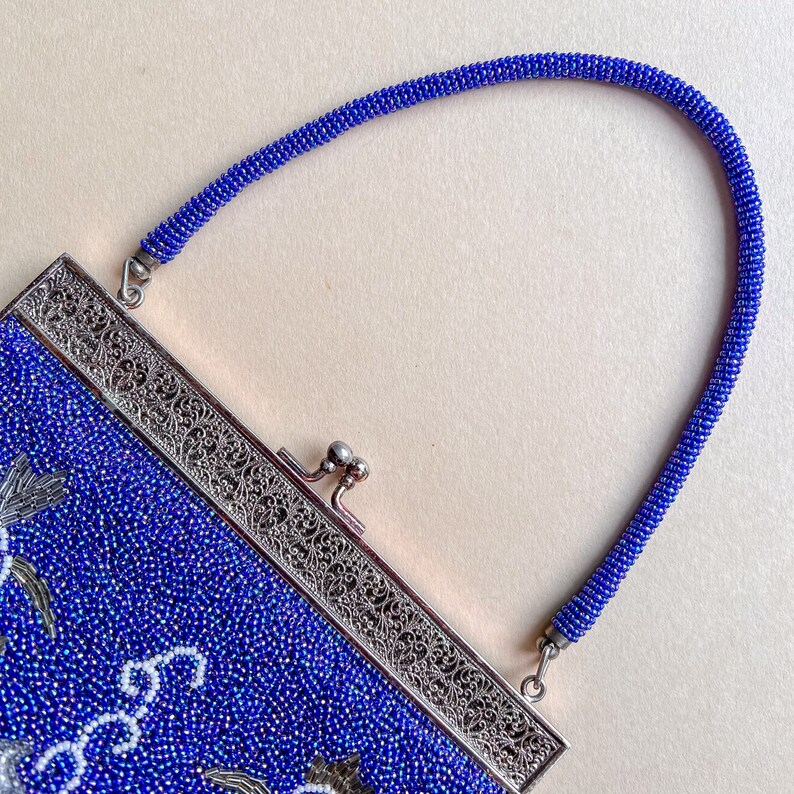 K&ouml;nnte beinhalten: Eine blaue Perlenhandtasche mit einem silbernen Verschluss und einem Perlenkettenriemen.