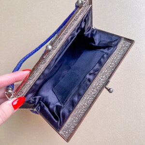 K&ouml;nnte beinhalten: Eine blaue Perlen-Abendtasche mit silbernem Metallrahmen und Satin-Futter. Die Tasche hat einen Verschluss und einen Kettenriemen.