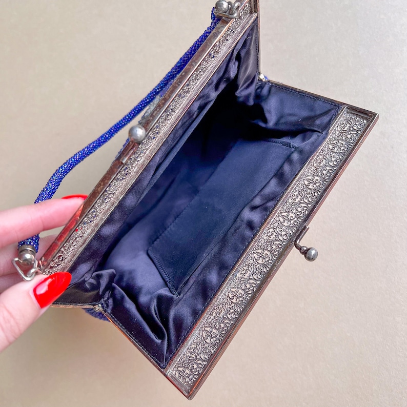 K&ouml;nnte beinhalten: Eine blaue Perlen-Abendtasche mit silbernem Metallrahmen und Satin-Futter. Die Tasche hat einen Verschluss und einen Kettenriemen.