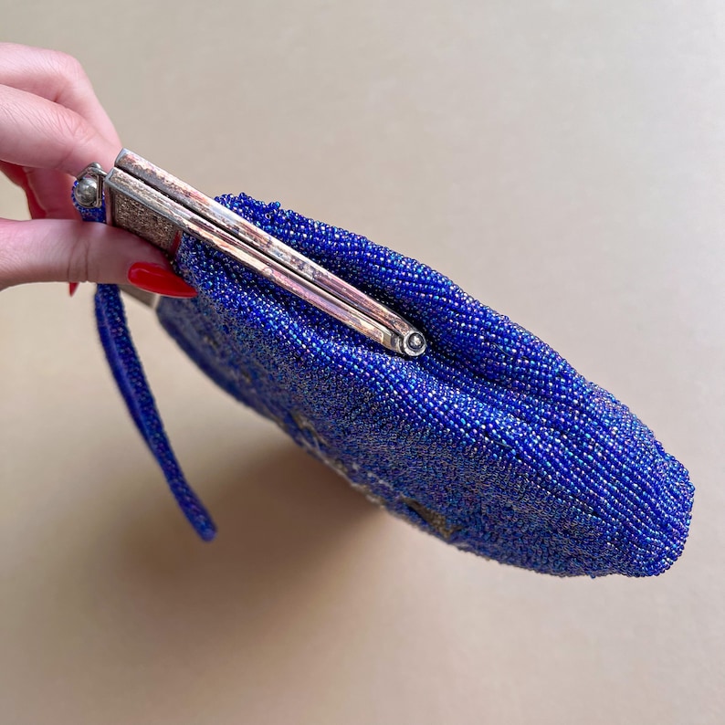 K&ouml;nnte beinhalten: Eine blaue Perlen-Abendtasche mit einem silbernen Verschluss. Die Tasche hat einen langen Riemen.