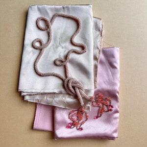 May include: A pink and beige silk scarf with a beaded necklace draped over it. The necklace has pink beads and a tassel.