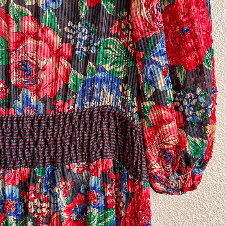K&ouml;nnte beinhalten: Ein schwarzes und rotes Blumenkleid mit geraffter Taille und langen &Auml;rmeln. Das Kleid ist aus einem durchsichtigen Stoff und hat einen Vintage-Stil.