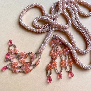 May include: A long pink beaded necklace with a tassel of pink and clear beads. The necklace is made of multiple strands of small beads and has a delicate, feminine look.