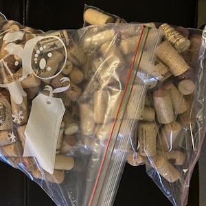 May include: Three clear plastic bags filled with a large quantity of used wine corks. The bags are sealed with red zipper closures.