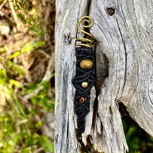 Könnte beinhalten: Ein schwarzes und goldenes Perlenhaarband mit einem spiralförmigen Draht-Akzent. Das Haarband ist um ein Stück verwittertes Holz gebunden.