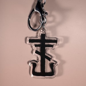 Peut inclure: Un porte-clés en acrylique transparent avec un motif de croix orthodoxe noire. Le porte-clés est doté d'un mousqueton et d'un anneau argentés. Le motif de la croix est une représentation stylisée de la croix orthodoxe orientale.