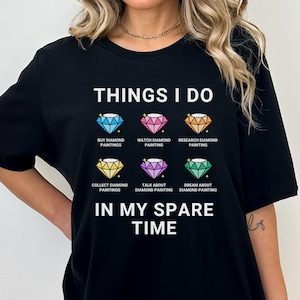 May include: A black t-shirt with the text "THINGS I DO" and a list of activities related to diamond painting. The activities include: buy diamond paintings, watch diamond painting, research diamond painting, collect diamond paintings, talk about diamond painting, and dream about diamond painting. The text "IN MY SPARE TIME" is below the list.