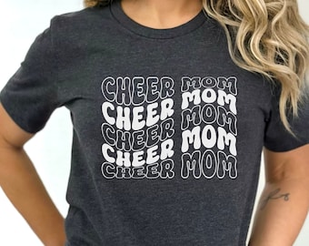 May include: A dark gray t-shirt with the text "CHEER MOM" repeated five times in a white retro font.