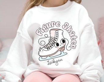 May include: White sweatshirt with a pink and white cartoon ice skate graphic and the text "Figure Skater" in a pink and white font. The name "Laibynn" is printed below the graphic.