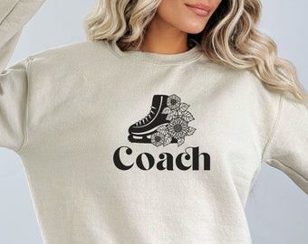 May include: A beige sweatshirt with a black graphic of an ice skate with flowers and the word "Coach" in a retro font.