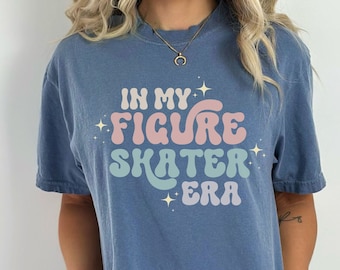 May include: A blue t-shirt with the text "In My Figure Skater Era" in a retro font with pink, blue, and green colors. The text is surrounded by small white stars.
