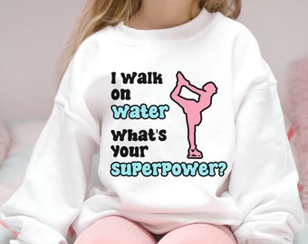May include: White sweatshirt with a pink figure skater silhouette and the text "I walk on water. What's your superpower?"