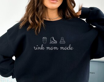 May include: Black sweatshirt with white text that reads "rink mom mode" and a graphic of a coffee cup, ice skate, and winter hat.