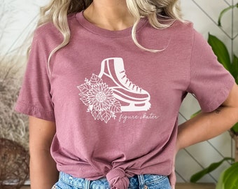 May include: A mauve t-shirt with a white graphic of a figure skate with a floral design and the text "figure skater".