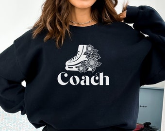 May include: Black sweatshirt with a white graphic of an ice skate with flowers and the word "Coach" underneath.
