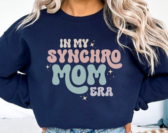 May include: Navy blue sweatshirt with the text "In My Synchro Mom Era" in a retro font with pastel colors and glitter accents.