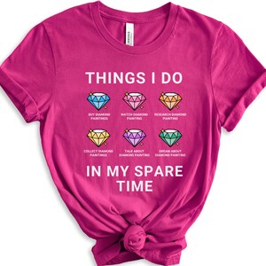 May include: A pink t-shirt with the text "THINGS I DO" and a list of activities related to diamond painting. The activities include: buy diamond paintings, watch diamond painting, research diamond painting, collect diamond paintings, talk about diamond painting, and dream about diamond painting. The text "IN MY SPARE TIME" is below the list.