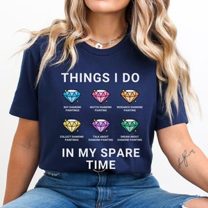 May include: A navy blue t-shirt with the text "THINGS I DO" and a list of activities related to diamond painting. The activities include "BUY DIAMOND PAINTINGS", "WATCH DIAMOND PAINTING", "RESEARCH DIAMOND PAINTING", "COLLECT DIAMOND PAINTINGS", "TALK ABOUT DIAMOND PAINTING", and "DREAM ABOUT DIAMOND PAINTING". The text "IN MY SPARE TIME" is printed below the list.
