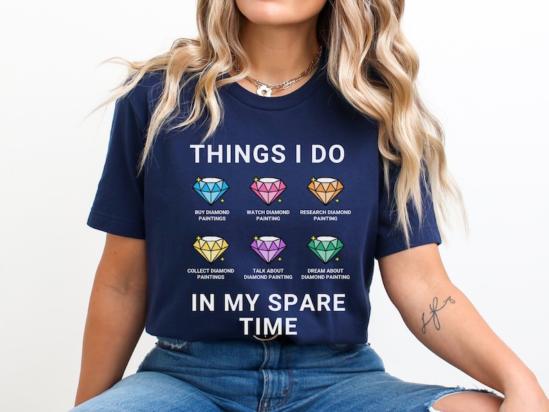 May include: A navy blue t-shirt with the text "THINGS I DO" and a list of activities related to diamond painting. The activities include "BUY DIAMOND PAINTINGS", "WATCH DIAMOND PAINTING", "RESEARCH DIAMOND PAINTING", "COLLECT DIAMOND PAINTINGS", "TALK ABOUT DIAMOND PAINTING", and "DREAM ABOUT DIAMOND PAINTING". The text "IN MY SPARE TIME" is printed below the list.