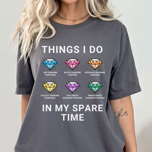 May include: A gray t-shirt with the text "THINGS I DO" and a list of activities related to diamond painting. The activities include: buy diamond paintings, watch diamond painting, research diamond painting, collect diamond paintings, talk about diamond painting, and dream about diamond painting. The text "IN MY SPARE TIME" is below the list.