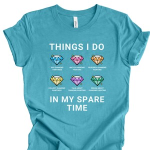 May include: A turquoise blue t-shirt with the text "THINGS I DO" and a list of activities related to diamond painting. The activities include: "Buy Diamond Paintings", "Watch Diamond Painting", "Research Diamond Painting", "Collect Diamond Paintings", "Talk About Diamond Painting", and "Dream About Diamond Painting". The text "IN MY SPARE TIME" is below the list.