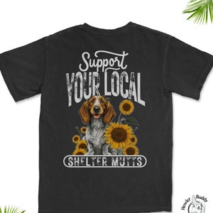 May include: Black t-shirt with a white graphic that says "Support Your Local Shelter Mutts". The graphic features a brown and white dog with sunflowers.
