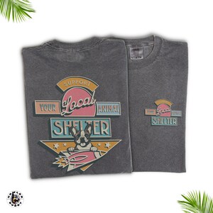 May include: Two charcoal gray t-shirts with a graphic supporting local animal shelters. The design features a French bulldog on a rocket, with text reading "Support Your Local Animal Shelter" in a retro style.