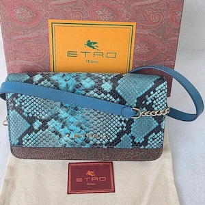 Puede incluir: Un bolso de hombro rectangular Etro Milano con cuerpo de piel con estampado de serpiente azul y negro y base con estampado de cachemira marrón oscuro. El bolso incluye una correa de piel azul, una cadena dorada, una caja y una bolsa protectora.