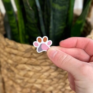 May include: A pink, brown, and gray paw print sticker. The sticker is on a white background.