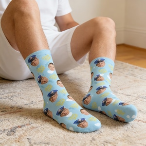 May include: Light blue socks with a repeating pattern of a man in a police hat and a child's face. The words "Damn Dad" are also printed on the socks. The socks are worn by a person sitting on a carpet.