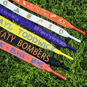 May include: A close-up shot of several shoelaces with various designs and text. The laces are in different colors, including red, white, yellow, purple, black, and orange. Text includes "WE WISH YOU MERRY CHRISTMAS", "RIP Papa 9/15/65-10/26/24", and "KATY BOMBERS".