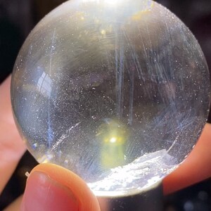 May include: A clear glass sphere with a light yellow glow in the center. The sphere has a smooth surface with visible scratches and imperfections.