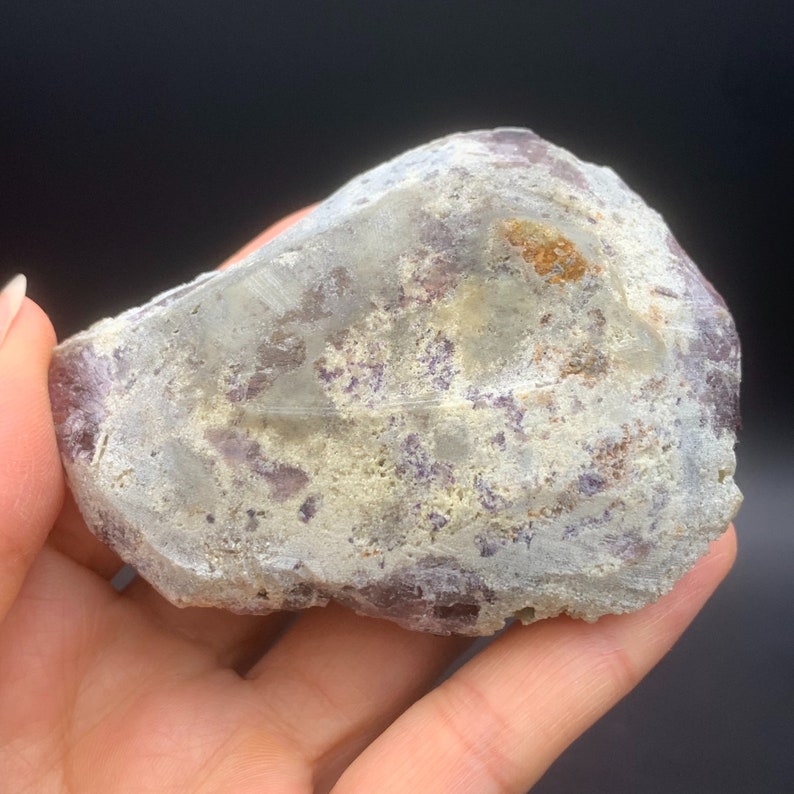 May include: A large, irregularly shaped, translucent purple and grey crystal with white and brown inclusions. The crystal has a rough, textured surface.