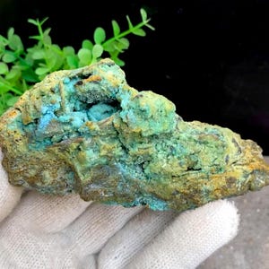 May include: A rough, green and brown rock with a blue-green mineral deposit. The rock has a rough, uneven surface and a variety of textures.